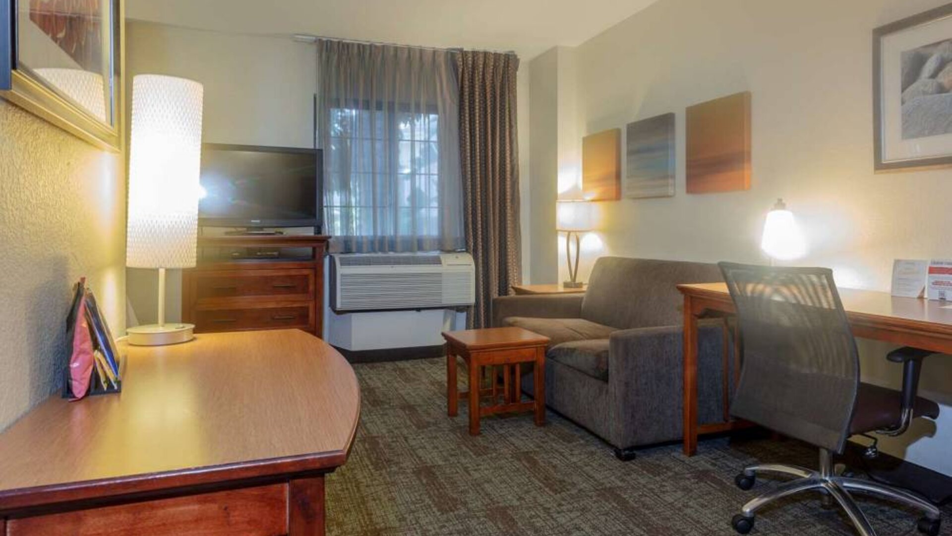 Guest room living area in Sonesta ES Suites Anaheim Resort Area, furnished with sofa and television, plus a workspace desk and chair.