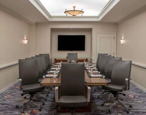 Sonesta Charlotte Executive Park meeting room, furnished with long table, a dozen leather swivel chairs, and a large, wall-mounted TV.