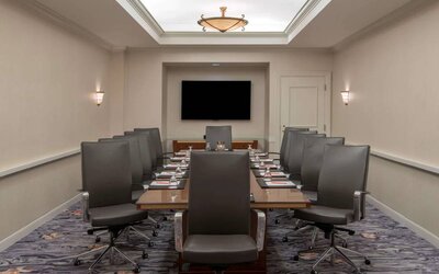 Sonesta Charlotte Executive Park meeting room, furnished with long table, a dozen leather swivel chairs, and a large, wall-mounted TV.