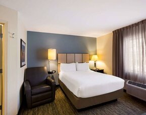 Sonesta Simply Suites St Louis Earth City double bed guest room, featuring armchair, window, and ensuite bathroom.
