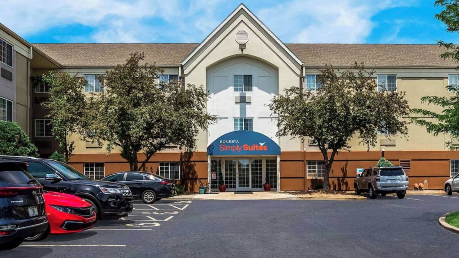 Sonesta Simply Suites St Louis Earth City’s exterior includes numerous parking spaces (including disabled spaces near the covered entrance) and trees.