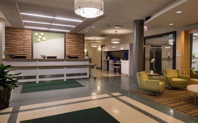 The hotel lobby has yellow armchairs, potted plants, and a business center workstation, in addition to the reception desk.