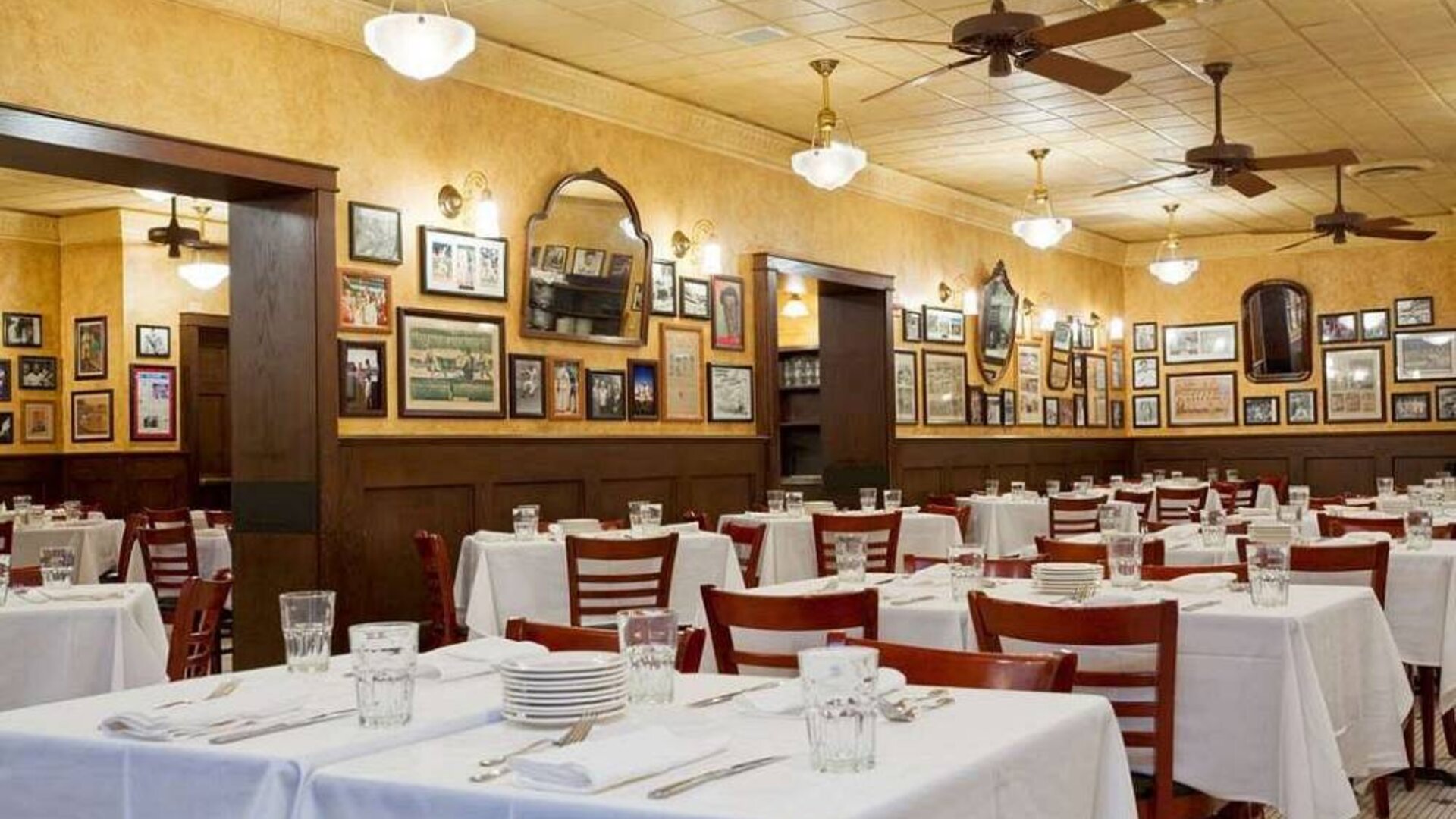 The hotel restaurant has white tablecloths, ceiling fans, and walls brimming with mirrors and photographs.
