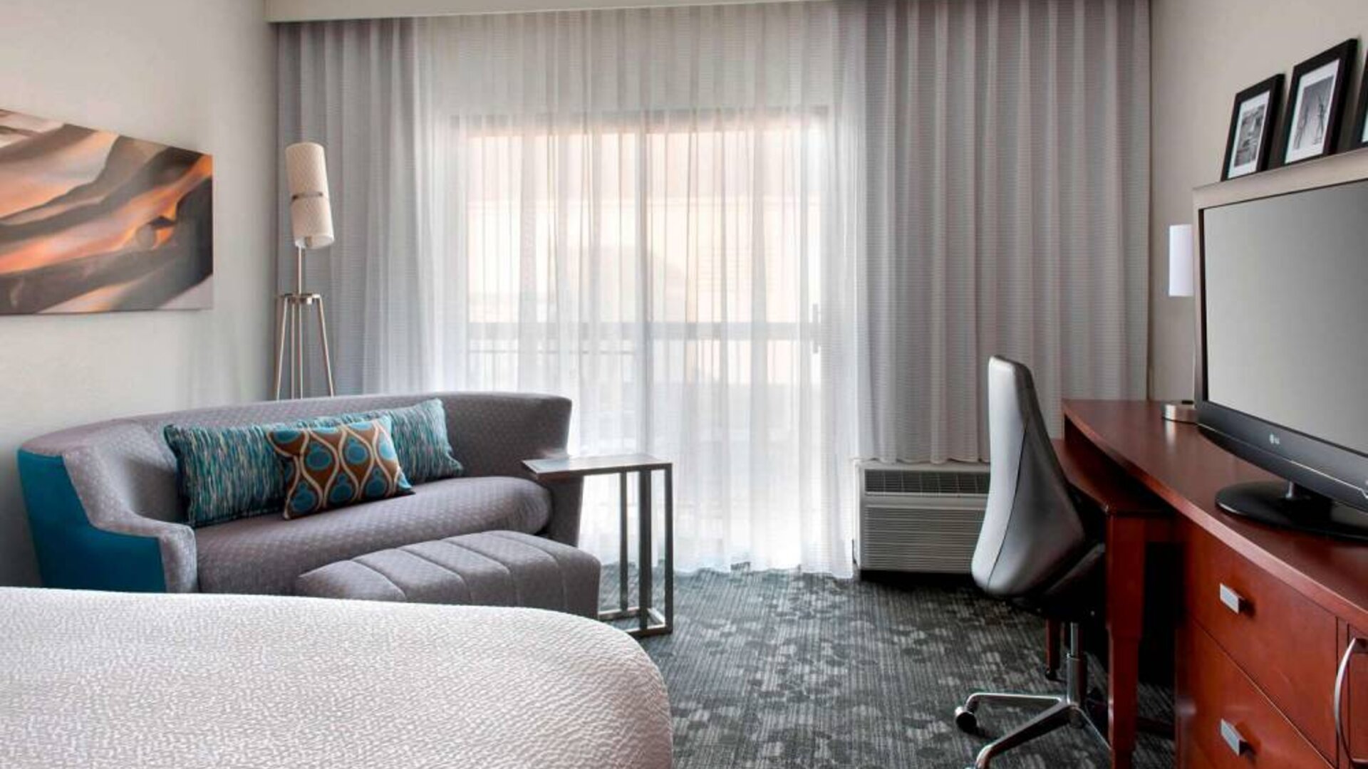 Double bed guest room in Sonesta Select Newport Middletown, featuring sofa, chair, window, and TV.