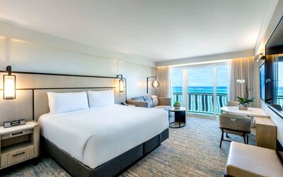 Royal Sonesta San Juan double bed guest room, furnished with table and chairs, sofa and coffee table, and a a balcony with ocean views.