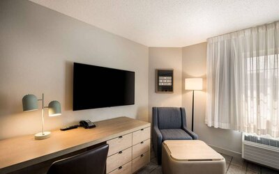 Sonesta Simply Suites Jersey City guest room workspace, including desk, chair, and lamp, with nearby TV and armchair.