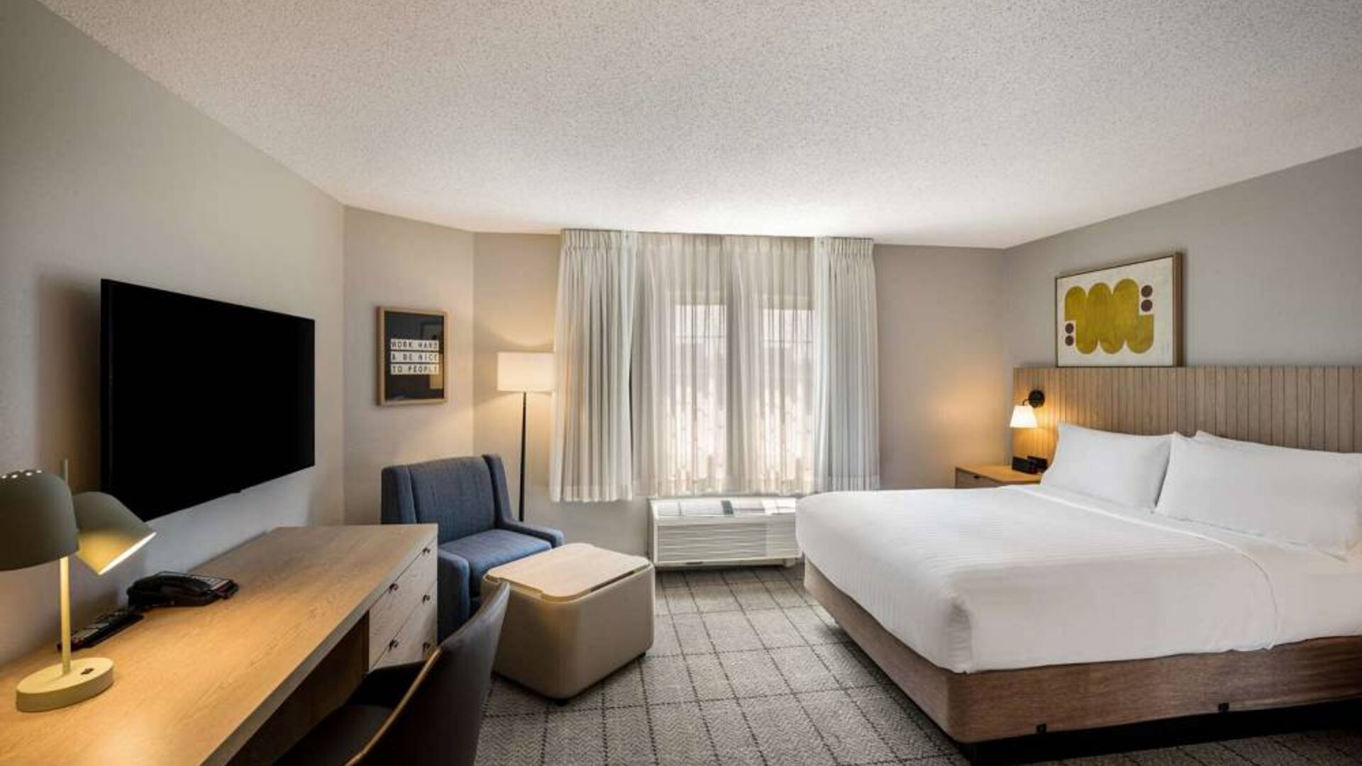 Sonesta Simply Suites Jersey City double bed guest room, featuring armchair, window, and widescreen television.