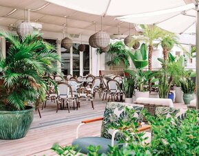 The hotel offers outdoor dining, with an abundance of plant life around the tables for four.