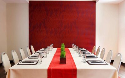 Meeting room in The Shelburne Sonesta New York, furnished with long table, 10 chairs around it, and a stark white and red color scheme.