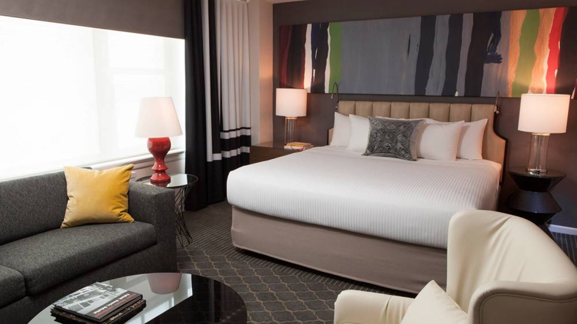 Double bed guest room in The Fifty Sonesta Select New York, with sofa, chair, coffee table, and large window.