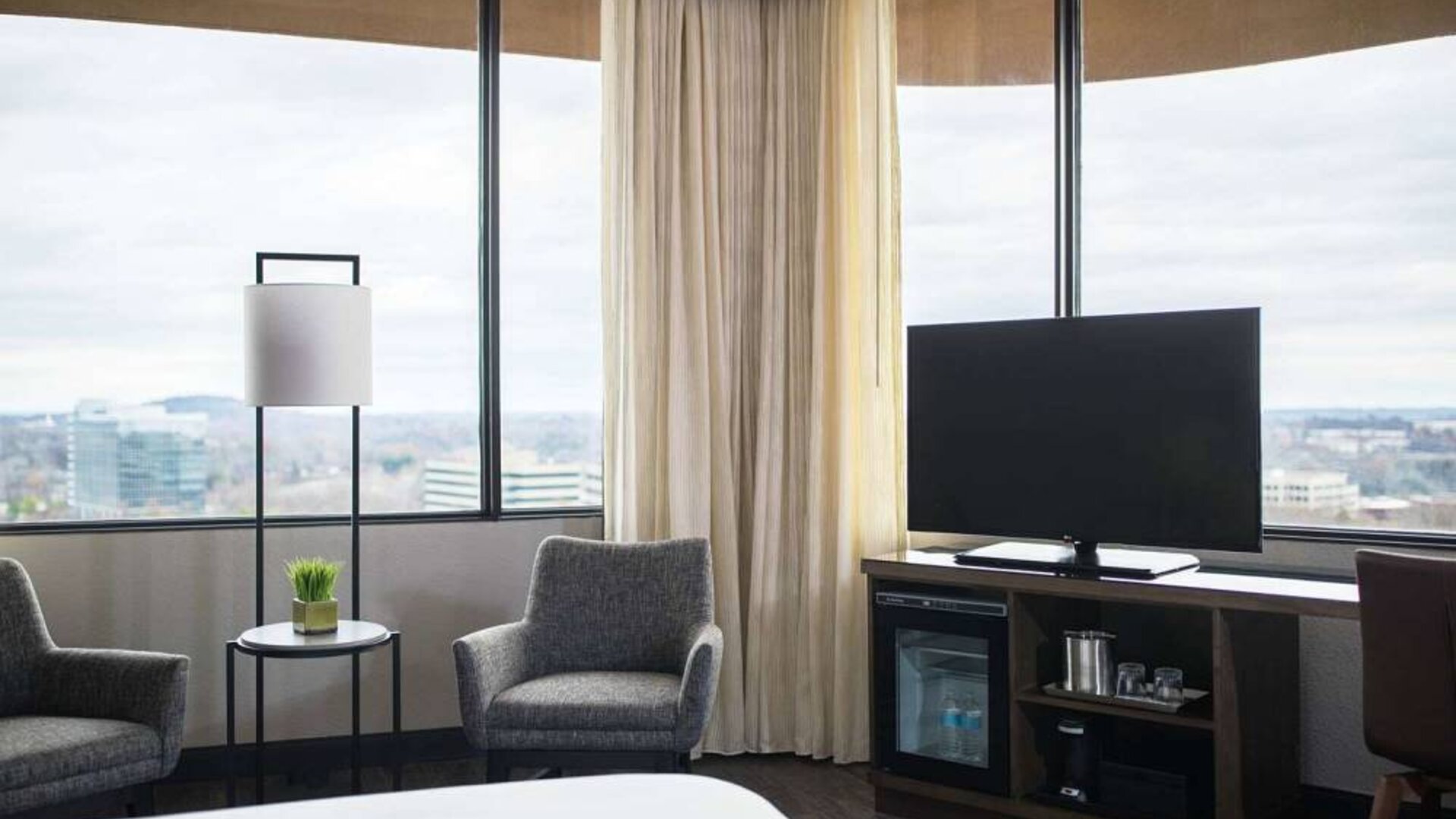 Sonesta Nashville Airport guest room, featuring widescreen television, chairs and a coffee table, and large windows.