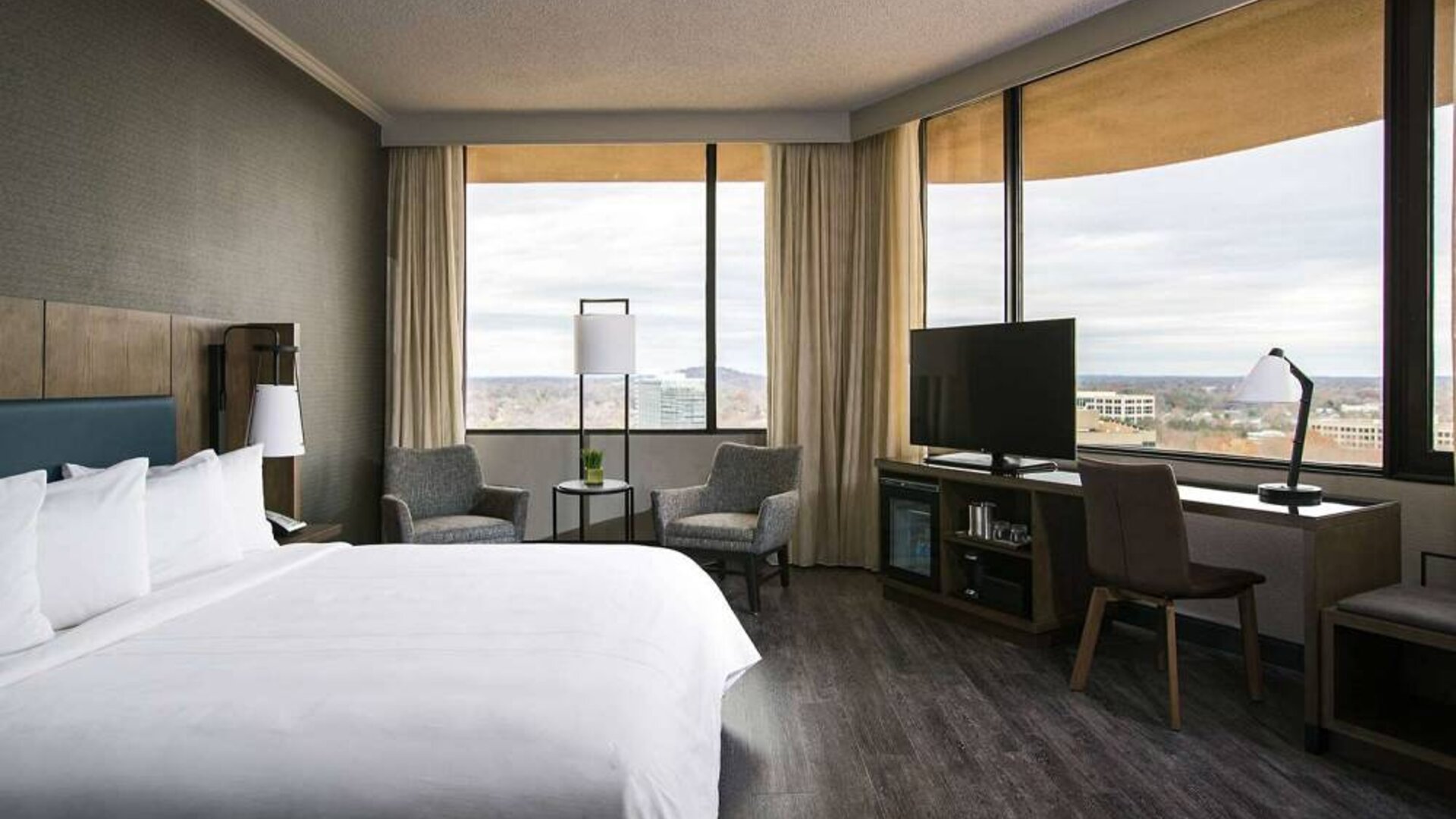 Double bed guest room in Sonesta Nashville Airport, furnished with chairs, coffee table, TV, large windows, and a workspace desk and chair.