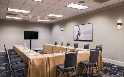 Meeting room in with tables arranged in a U-shape facing  large TV, plus a large artistic photograph of a horse on the wall.