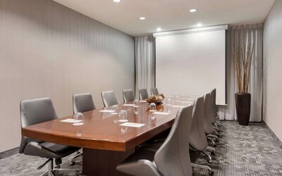 Sonesta Select Tempe Downtown meeting room, featuring long wooden table, a dozen swivel chairs, and a projector screen.