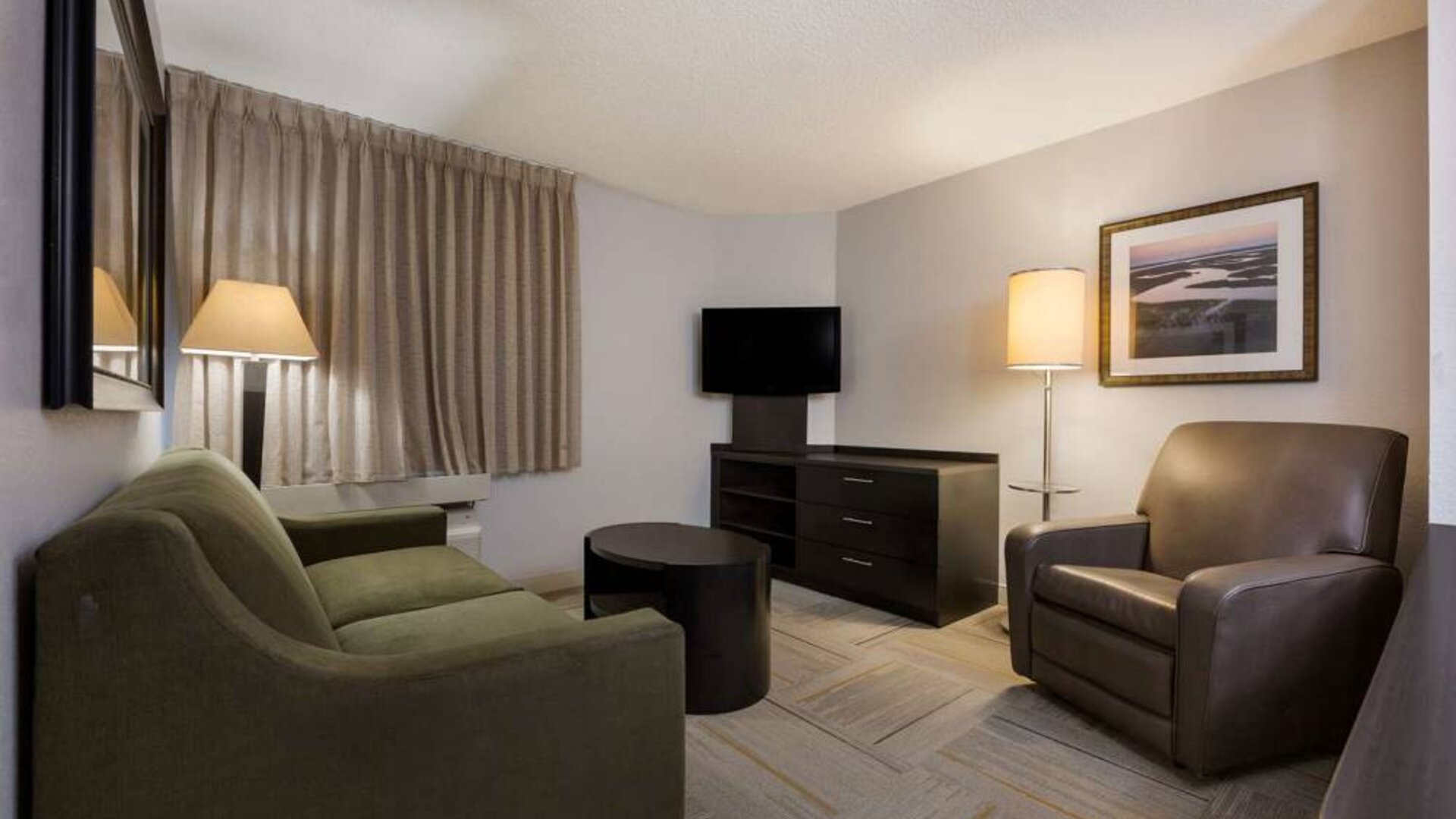 Guest room lounge in Sonesta Simply Suites Huntsville Research Park, furnished with sofa, armchair, coffee table, and window.