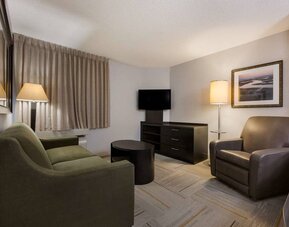 Guest room lounge in Sonesta Simply Suites Huntsville Research Park, furnished with sofa, armchair, coffee table, and window.