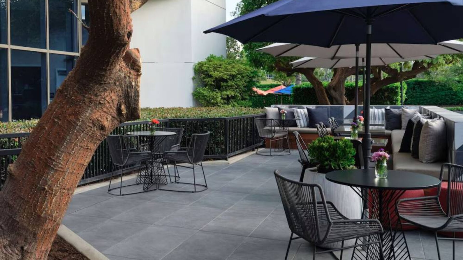 The patio at Sonesta Irvine features sofa seating alongside tables and chairs (shade available), with flowers on each table.