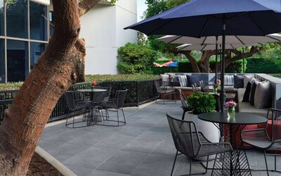 The patio at Sonesta Irvine features sofa seating alongside tables and chairs (shade available), with flowers on each table.
