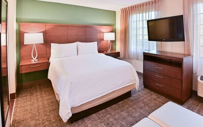 Double bed guest room in Sonesta ES Suites Fort Lauderdale Plantation, featuring bedside lamps, windows, and a large TV.