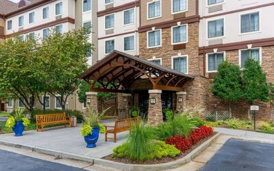 The hotel’s exterior has a pair of benches beside the covered entrance, with flowerbeds, bushes, and trees nearby.