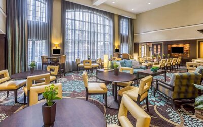 The hotel’s breakfast area has a carpeted floor, range of table sizes, seating from normal chairs to tall stools and armchairs, high ceilings and large windows, plus multiple TVs.