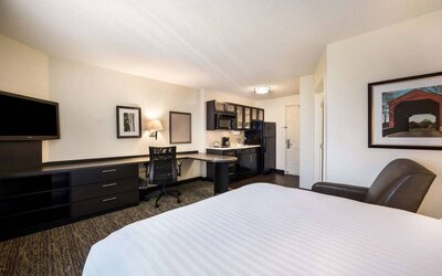 Sonesta Simply Suites Atlanta Gwinnett Place double bed guest room, with workspace desk and chair, kitchen, armchair, and a widescreen TV.