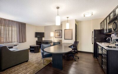 Sonesta Simply Suites Parsippany Morris Plains guest room living area, furnished with table and chairs, sofa, window, and TV.