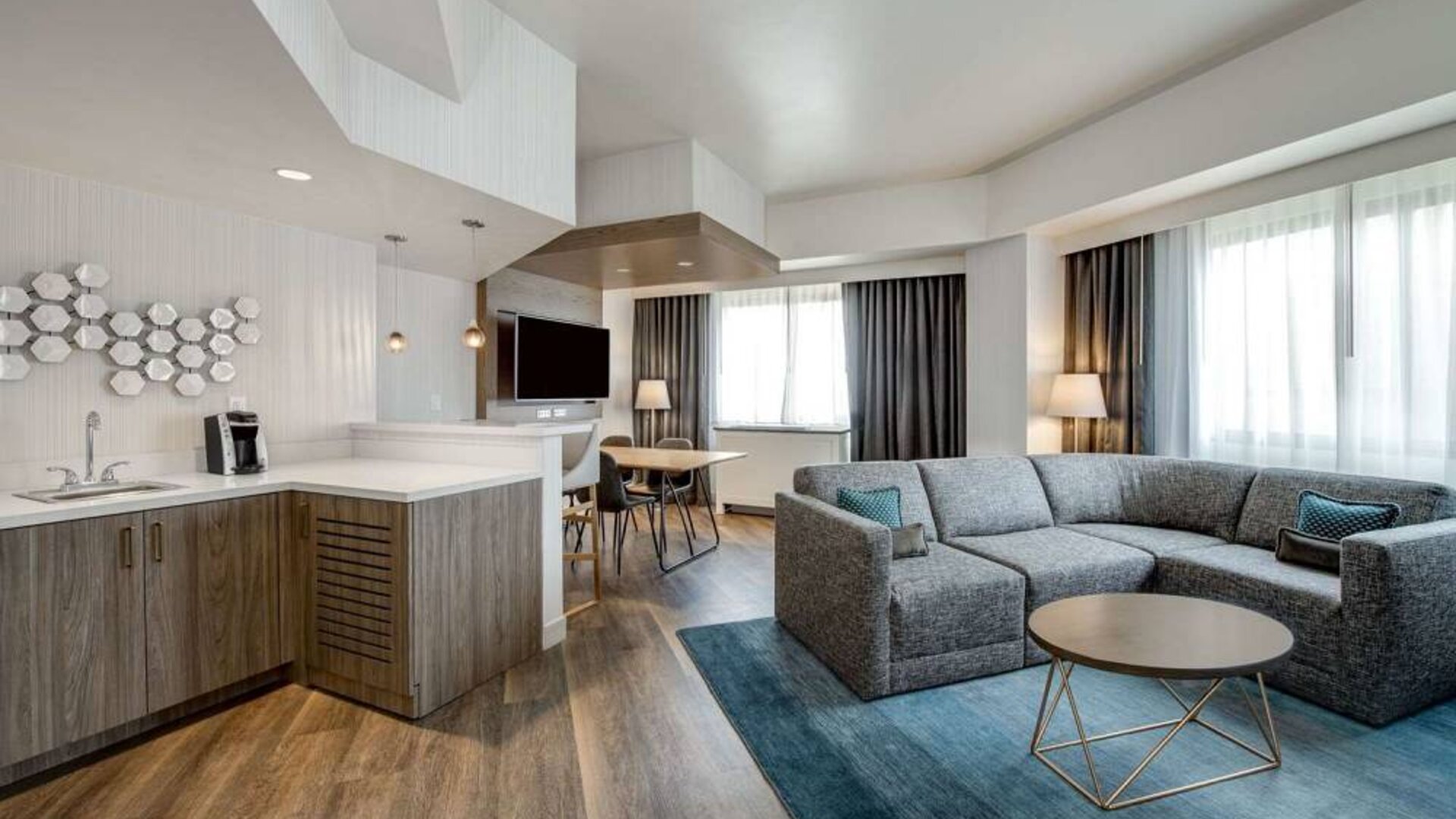 Guest room living area in Sonesta Columbus Downtown, including corner sofa and coffee table, large windows, and a TV with table and chairs nearby.