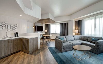 Guest room living area in Sonesta Columbus Downtown, including corner sofa and coffee table, large windows, and a TV with table and chairs nearby.
