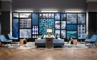 The hotel’s lobby lounge is furnished with comfortable chairs and sofa seating, with coffee tables and a wall filled with predominantly architecture-themed artwork.