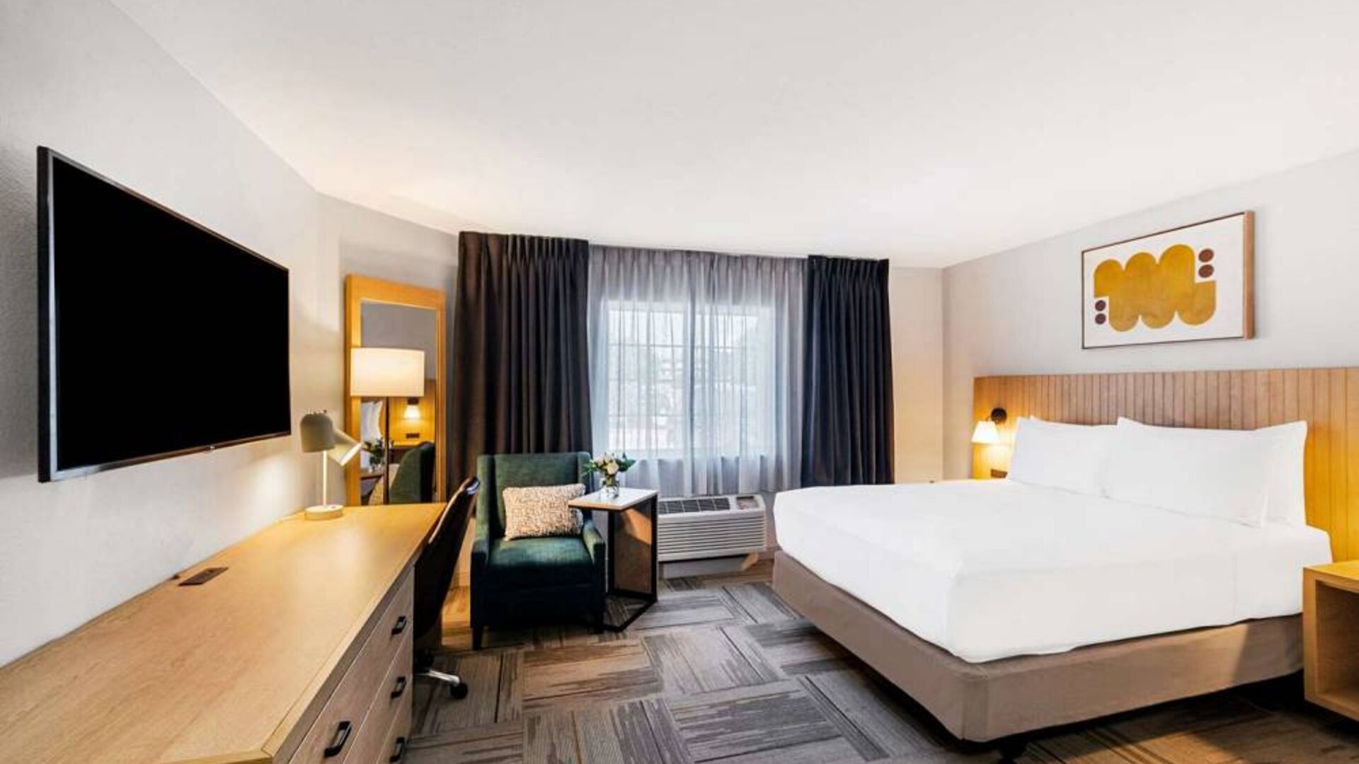 Double bed guest room in Sonesta Simply Suites Austin South, including window, armchair, and a widescreen television.