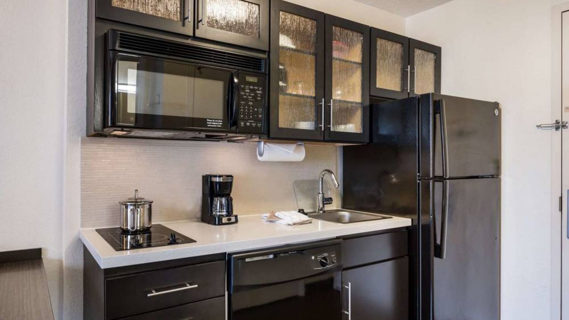 Sonesta Simply Suites Austin The Domain Area guest room kitchen, with fridge-freezer, sink, microwave, and hob.