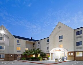 The hotel’s exterior includes parking close to the front door, benches, potted plants, plus bushes, trees, and flowers.