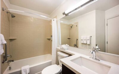 Guest bathroom in Sonesta Simply Suites Plano Frisco, including mirror and sink, lavatory, and bath equipped with a shower.