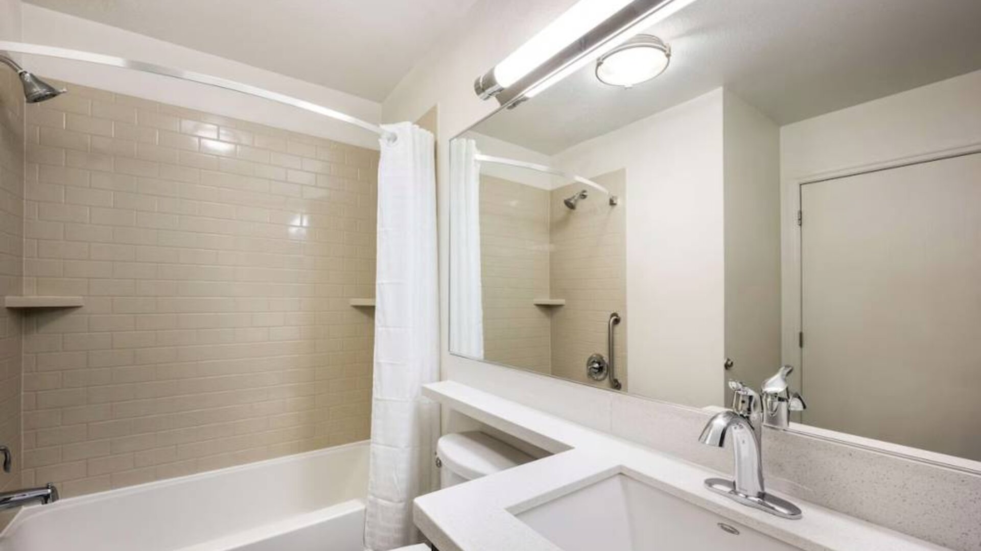 Guest bathroom in Sonesta Simply Suites Dallas Las Colinas, featuring bath with a shower, mirror, sink, and lavatory.