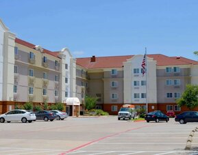 The hotel’s exterior has ample parking for guests, a US flag fluttering on a flagpole, and abundant greenery.