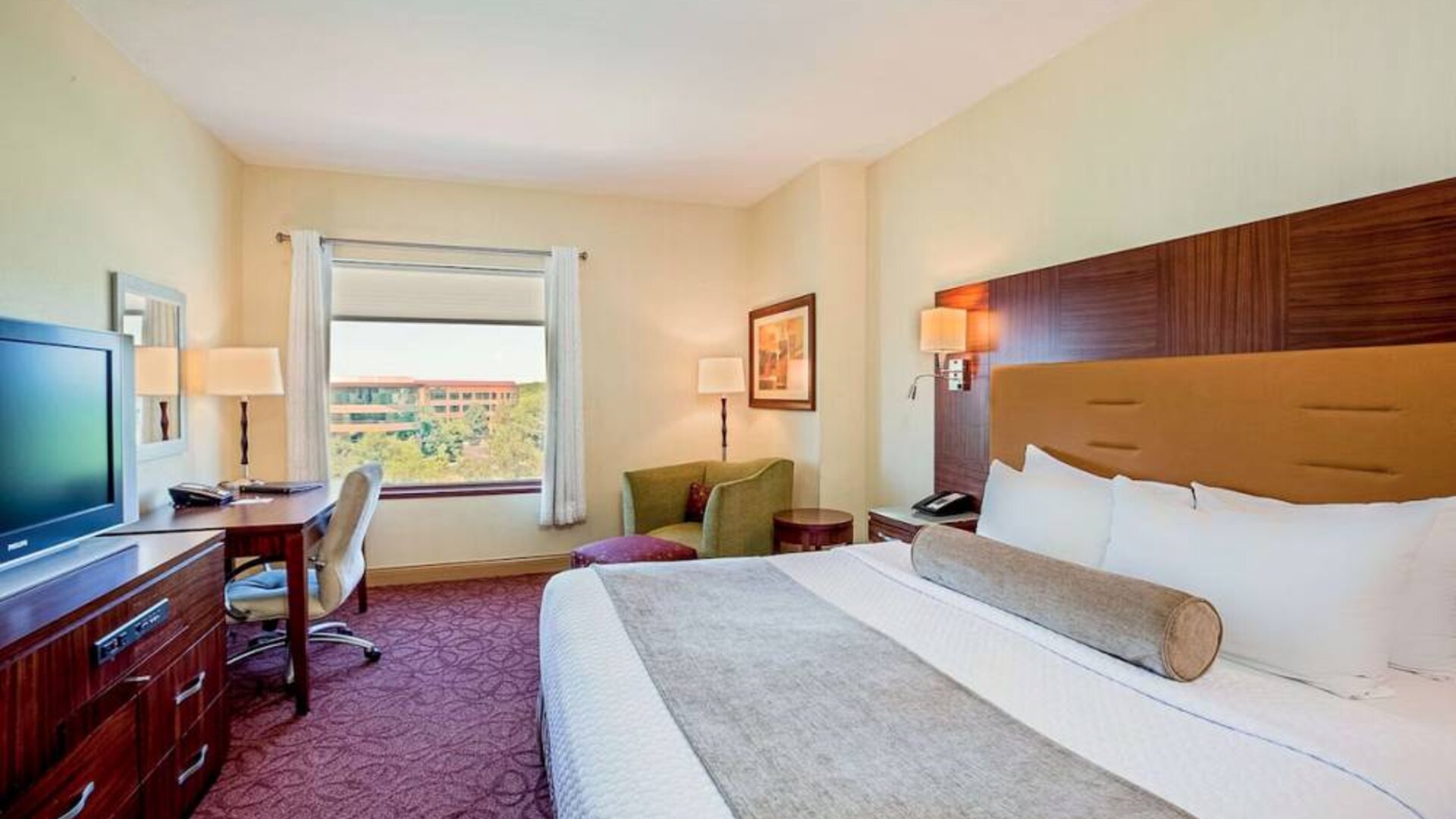 Sonesta Milwaukee West Wauwatosa double bed guest room, including armchair, TV, desk, chair, and window.