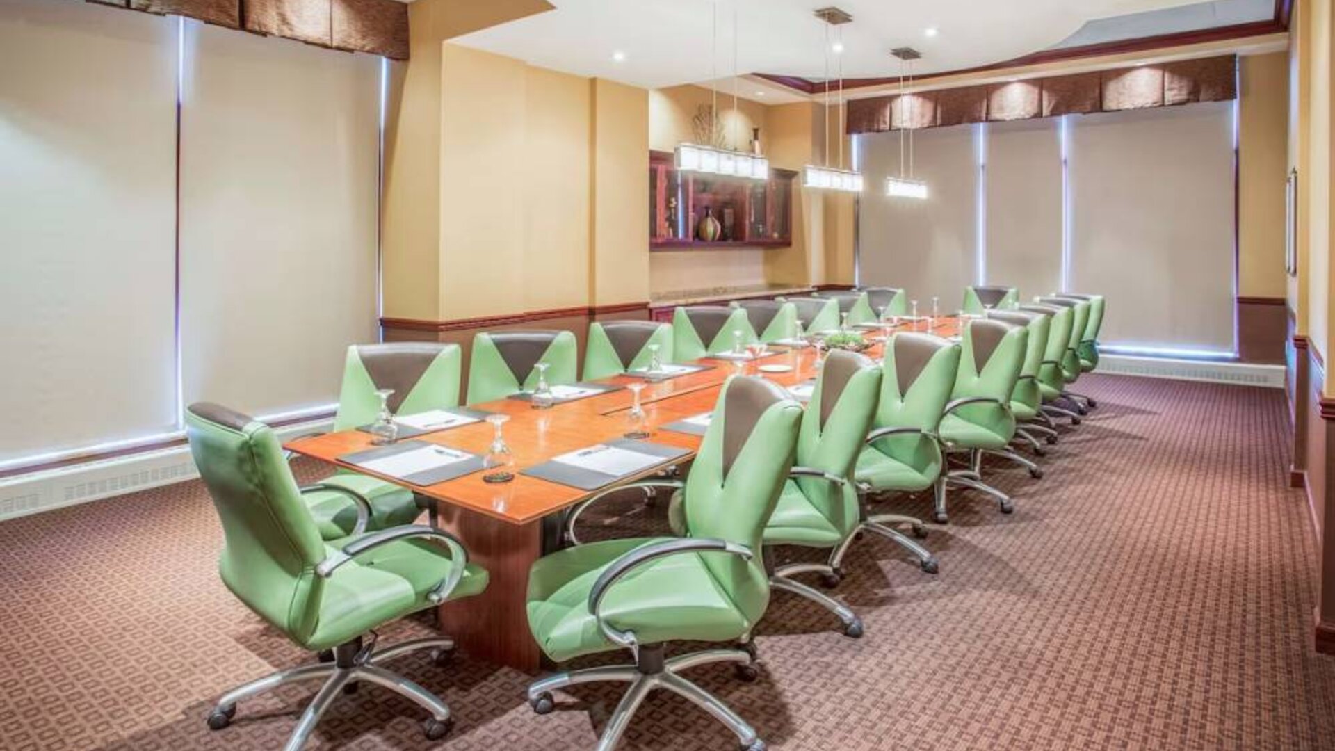 Hotel meeting room, furnished with a long wooden table and 18 green swivel chairs.