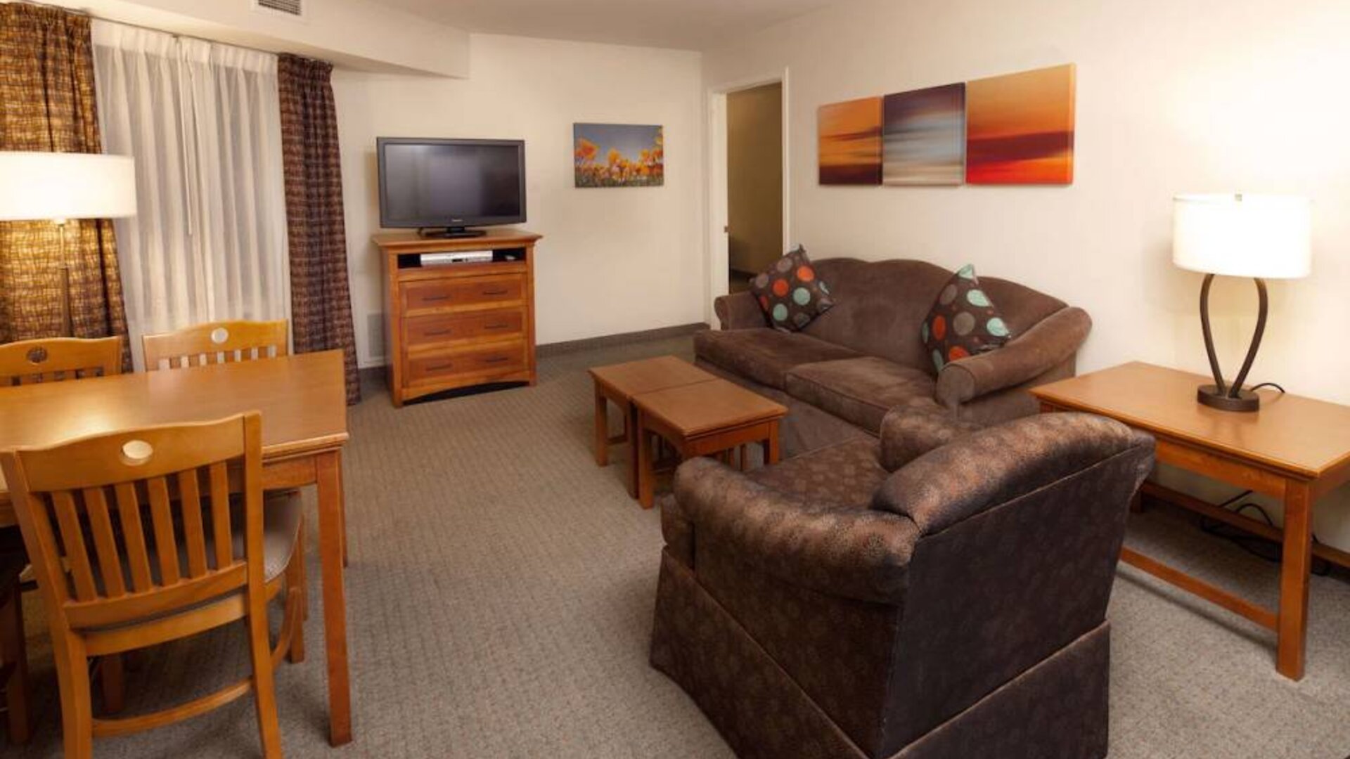 Sonesta ES Suites Dallas Las Colinas guest room living area, furnished with table and chairs, sofa, armchair, coffee tables, and TV.