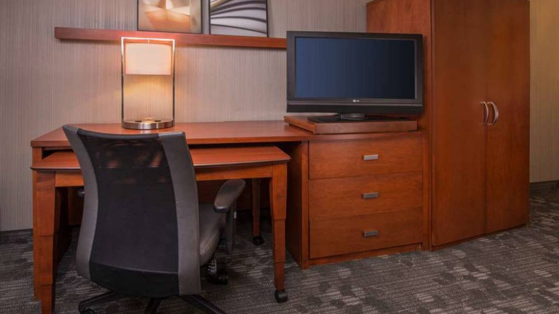 Sonesta Select Columbia guest room workspace, featuring desk, chair, and lamp, with a nearby TV.