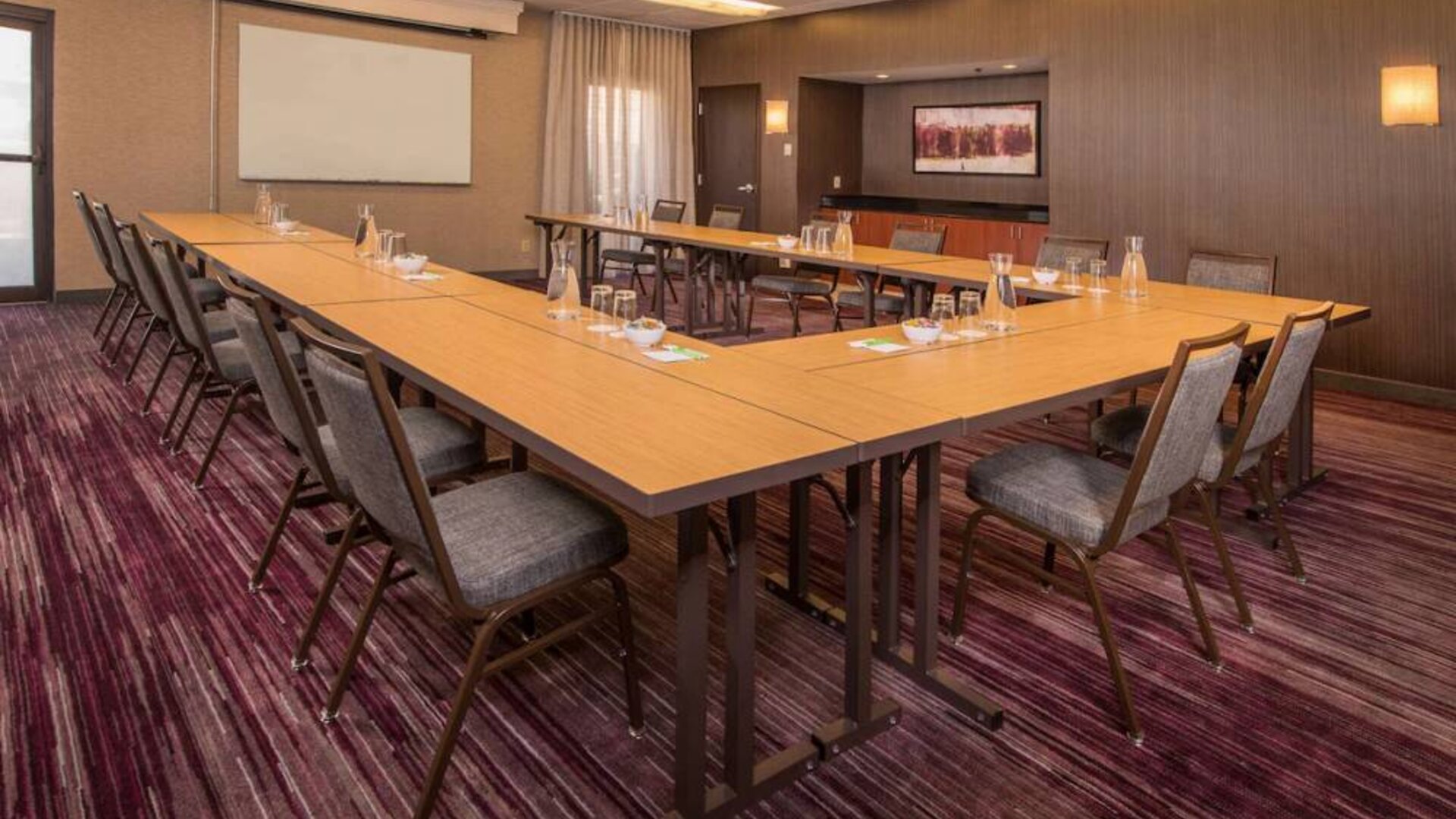 Meeting room in Sonesta Select Columbia, with tables arranged in a U-shape, seating for over a dozen attendees, and a whiteboard.
