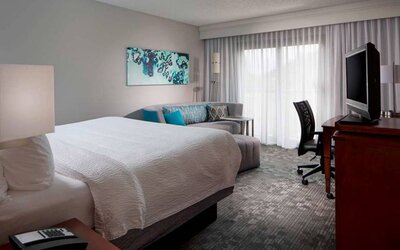 Sonesta Select Boca Raton double bed guest room, including sofa, window, TV, and a workspace desk and chair.