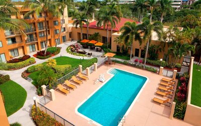 Sonesta Select Boca Raton’s outdoor pool is equipped with a lift, and has sun loungers by the side plus pleasant greenery beyond the fence.