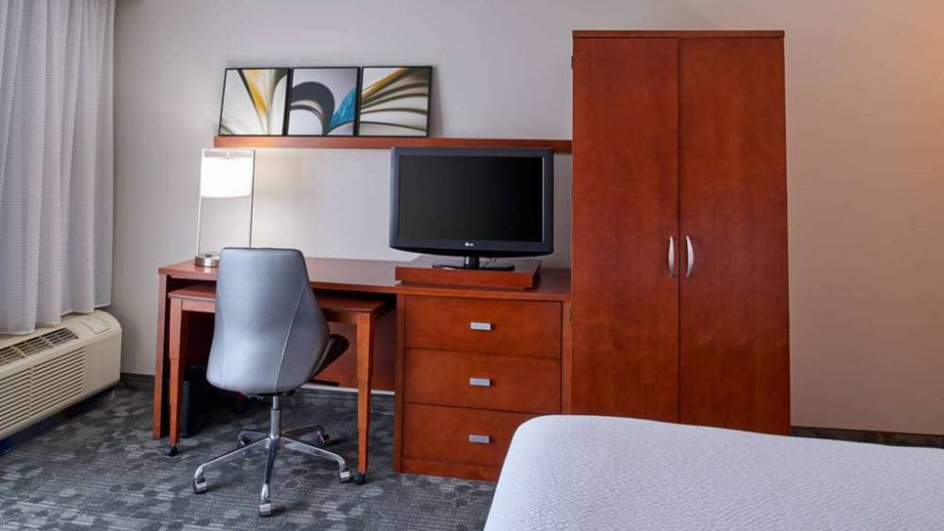 Sonesta Select Indianapolis Carmel guest room workspace, furnished with bed and TV, plus desk, chair, and lamp.