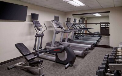 The hotel fitness center is equipped with free weights, a range of exercise machines, and a wall-mounted TV.