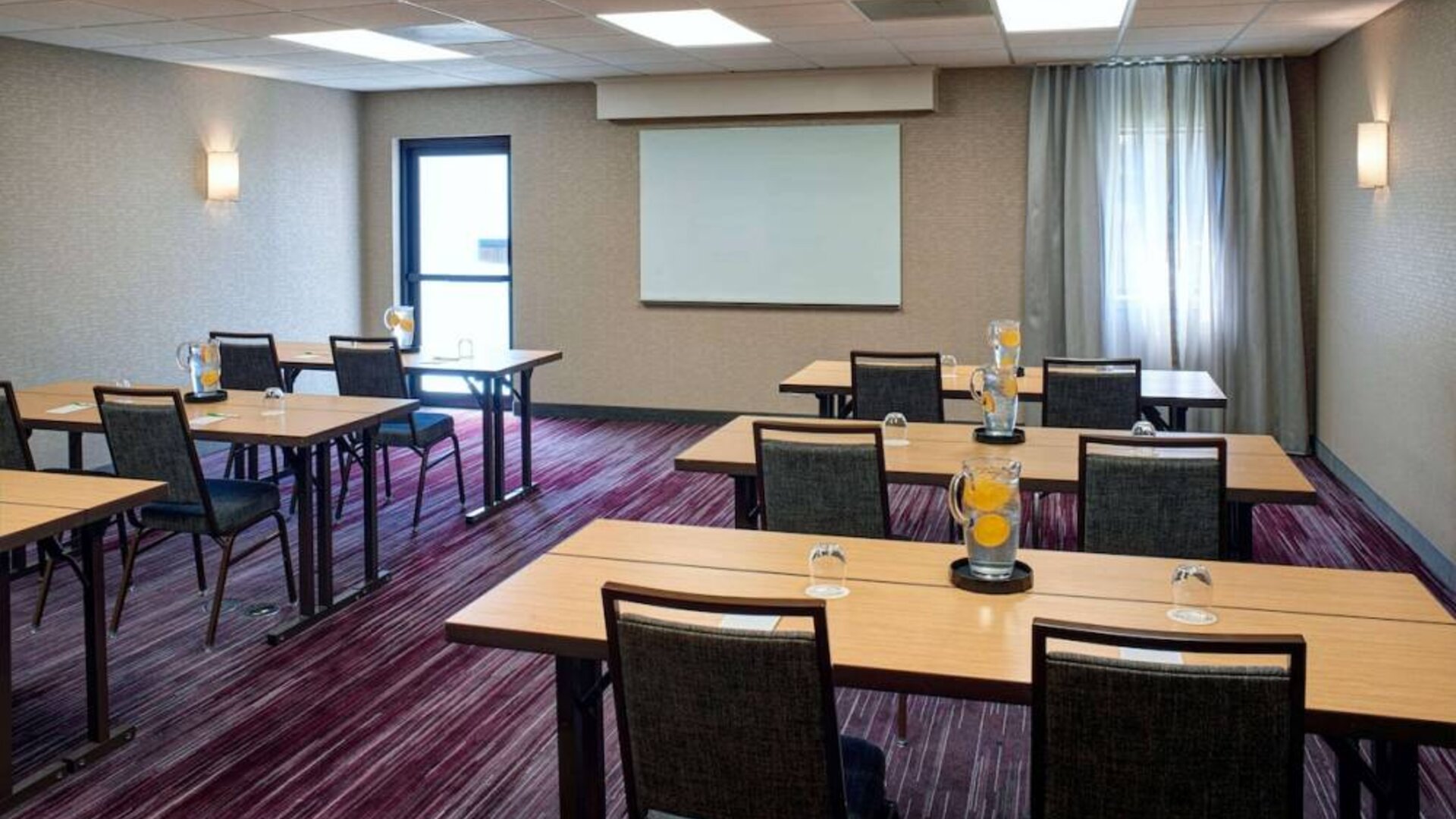Hotel meeting room with tables, in a classroom format, facing a whiteboard and window.