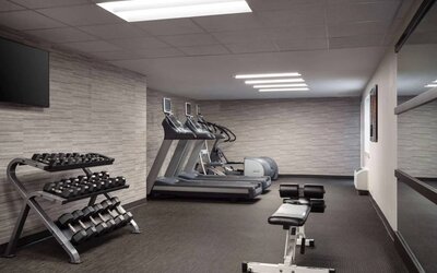 The fitness center at Sonesta Select Phoenix Camelback is equipped with free weights, a range of exercise machines, and a wall-mounted television.