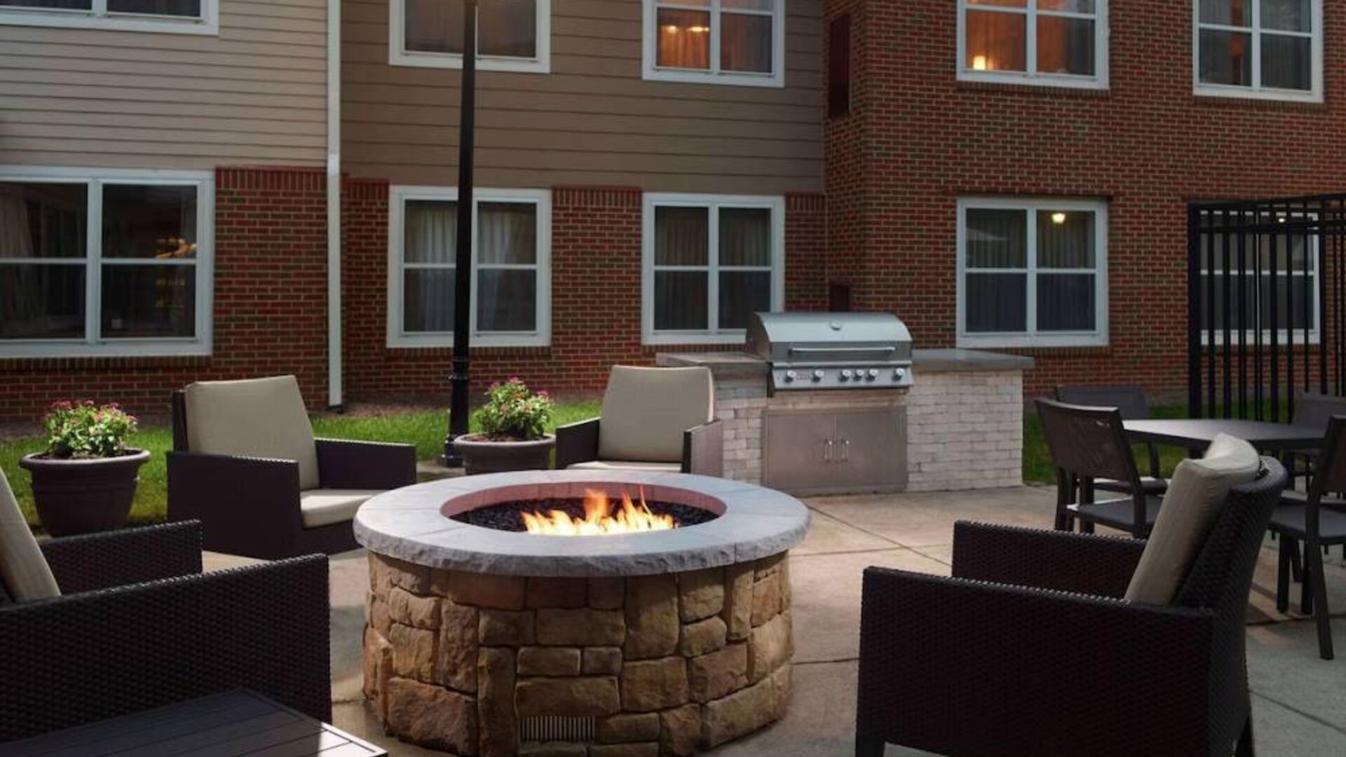 The fire pit at Sonesta ES Suites Raleigh Cary has armchairs around it, a barbecue, and potted plants.