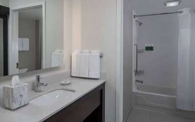 Guest bathroom in Sonesta ES Suites Fairfax Fair Lakes, with shower-equipped bath, mirror, and sink.