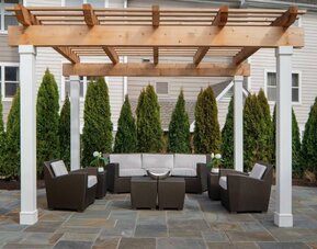 Sonesta ES Suites Fairfax Fair Lakes’s patio is furnished with armchair and sofa seating, plus coffee tables and nearby greenery.